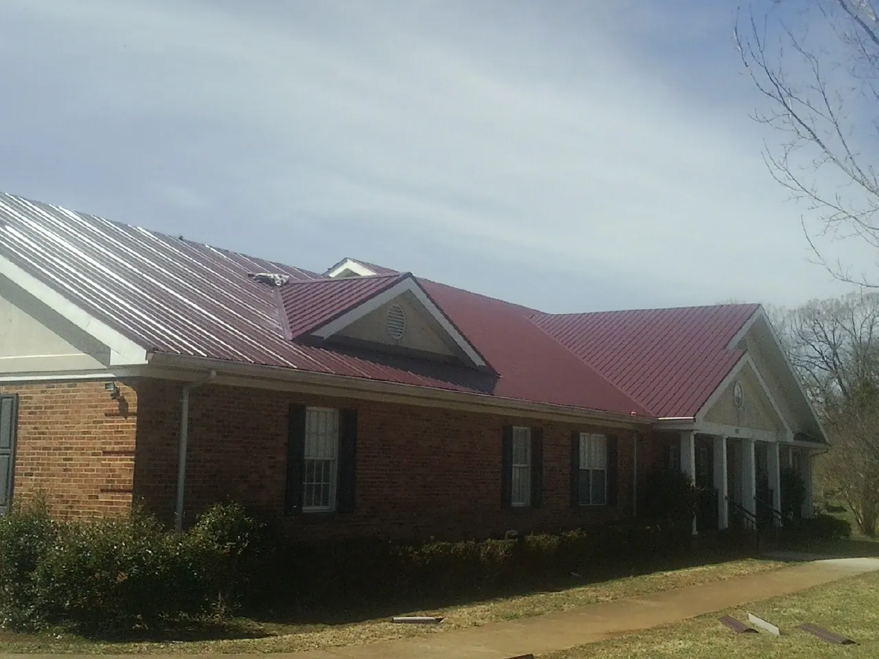 Red metal roof with gabled entries on a long brick building, from a Hail Damage Roof Repair job in Ayden