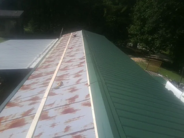 Old rusted panels beside newly installed green metal roofing — Wind Damage Roof Repair by Roofing Brothers in Ayden