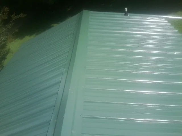 New green metal panels meeting at the ridge of a roof — Flat Roof Repair work by our crew in Ayden